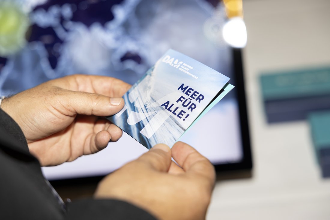 Eine Person hält einen Flyer mit der Aufschrift "Meer für alle" in den Händen.