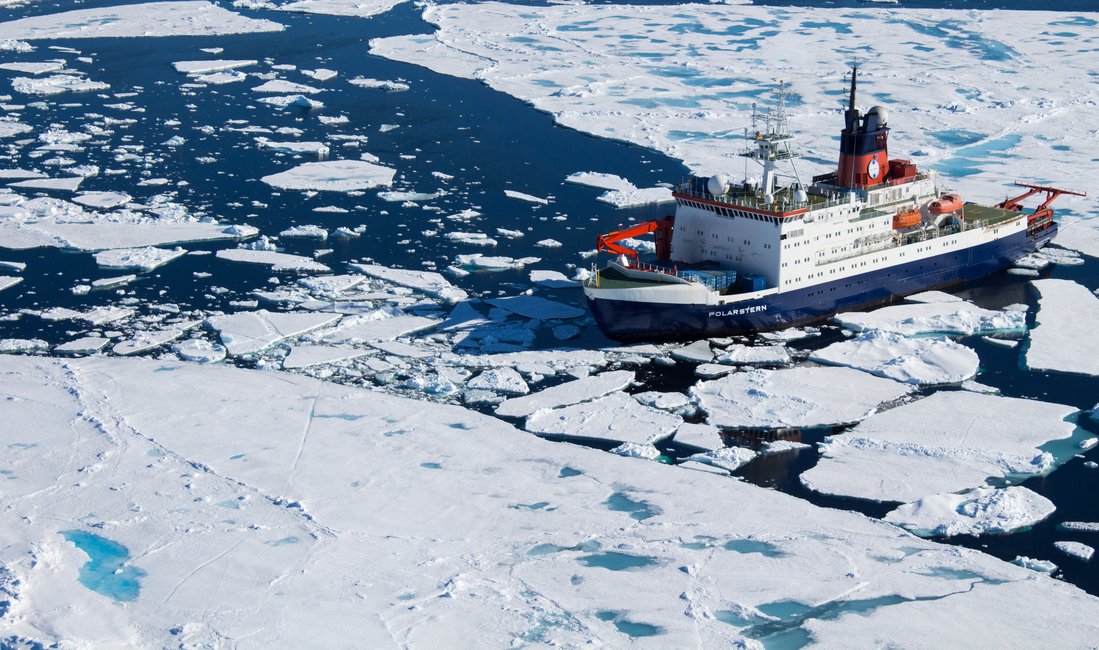 Der Forschungseisbrecher Polarstern fährt zwischen Eisschollen auf glattem Meer.