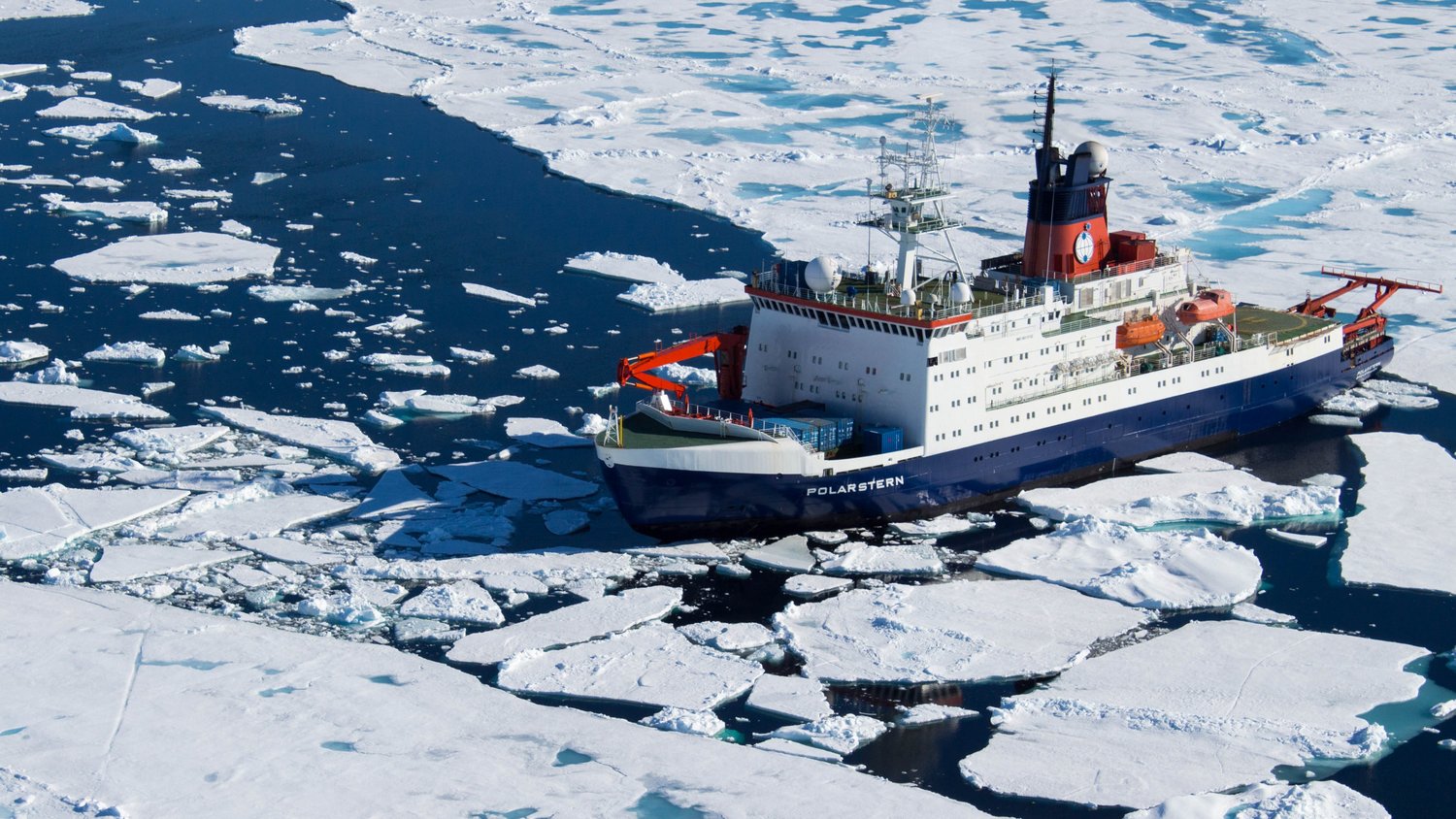Der Forschungseisbrecher Polarstern fährt zwischen Eisschollen auf glattem Meer.