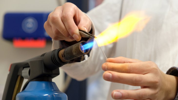 A small glass tube is formed on a burner.