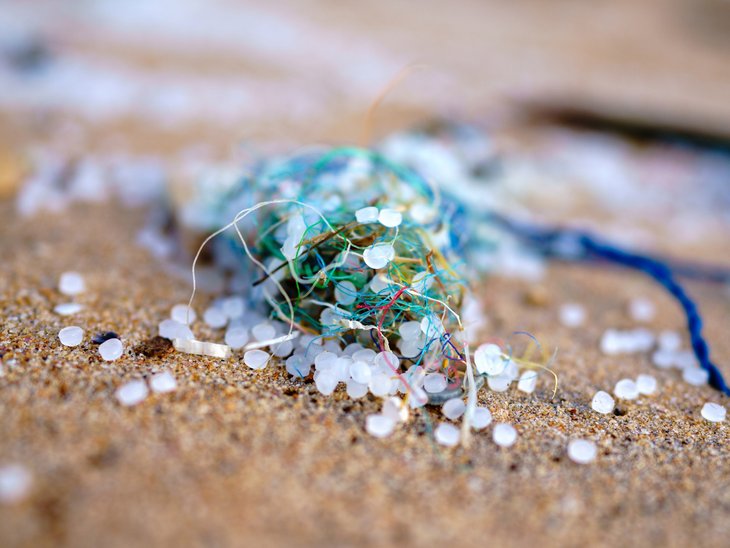 Der Rest eines Fischernetzes liegt am Strand. Darauf und daneben sind weiße Plastipellets verteilt.