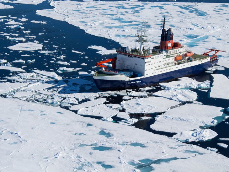 The research icebreaker Polarstern travels between ice floes of the Arctic sea ice on a smooth sea.