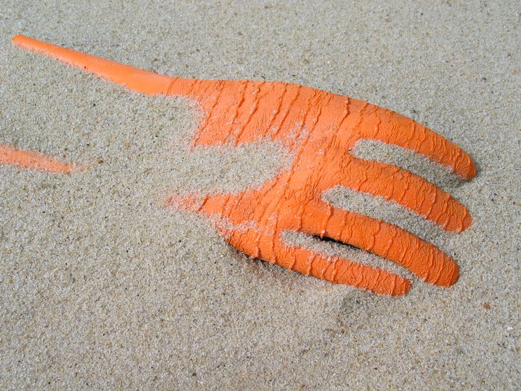 Abfall aus der Fischerei: Orangefarbener Gummihandschuh liegt am Sandstrand, Sylt, Nordsee.
