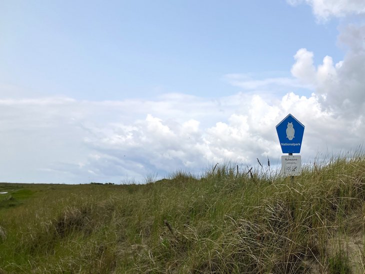  A blue sign with a white owl marks the national park in the dunes of Baltrum, which can be seen in the background.